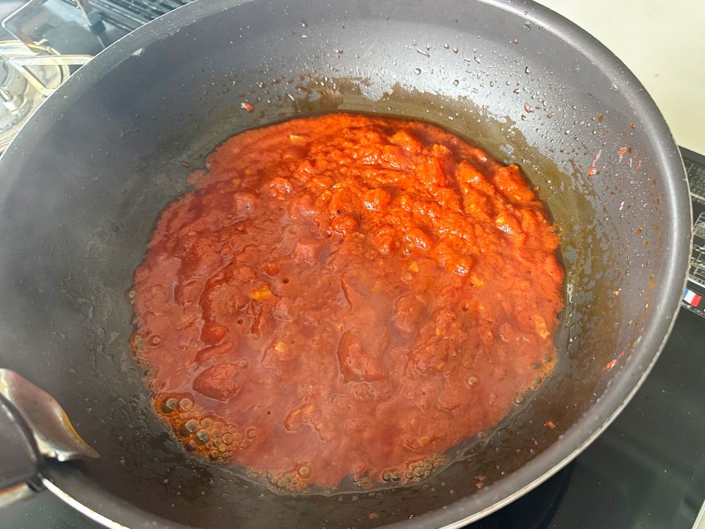 トマト水煮を加えて木べらで軽くつぶしながら混ぜる。フツフツしたら弱火にして水分が飛び、ポテッとするまで煮る。目安は15分。
