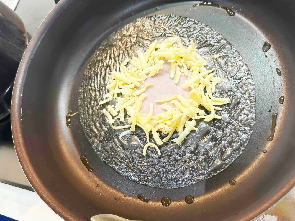 中央にハムをのせ、チーズで土手を作り、たまごを割り入れる。水大さじ1くらいを加えてふたをし、たまごを好みの固さまで焼く。