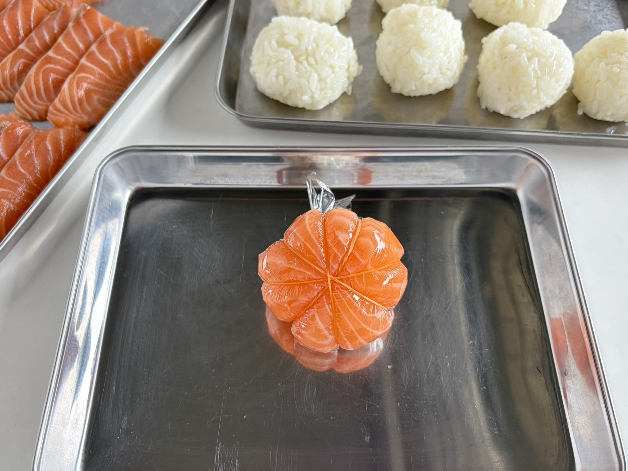 ラップを絞った面で輪ゴムを十字にかける。放射状になるように、もう１本の輪ゴムをかけ、かぼちゃの線をつける。１個につき輪ゴムを２本使う。