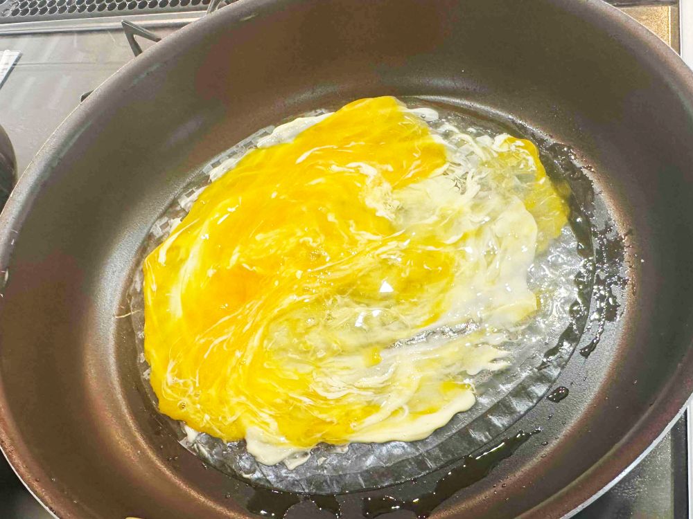 フライパンにオリーブオイル大さじ1/2を入れ、ライスペーパーを1枚のせ、マヨネーズ半量を塗り、たまごを割り入れる。スプーンなどでたまごをつぶして全体に広げる。